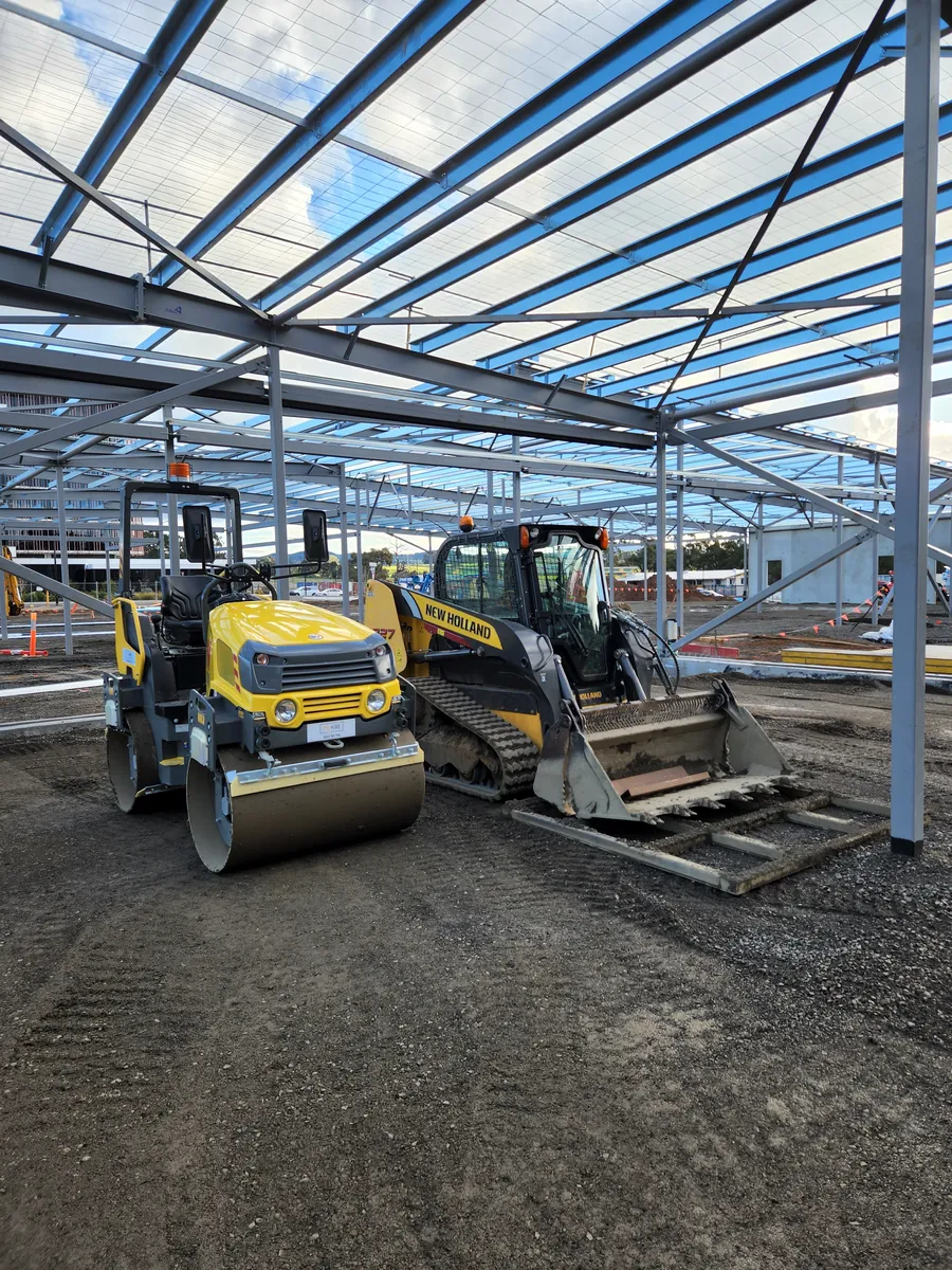 Roller and tracked skid steer preparing ground under a steel building frame